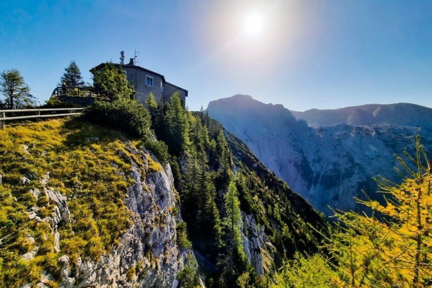 A mountain house on a cliff, surrounded by trees and a clear sky. 5