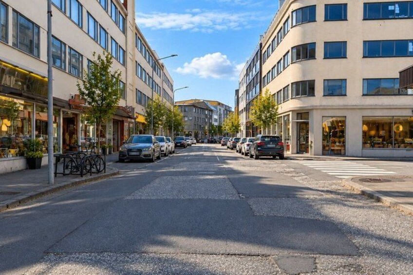 A street lined with modern buildings, parked cars, and trees. 5