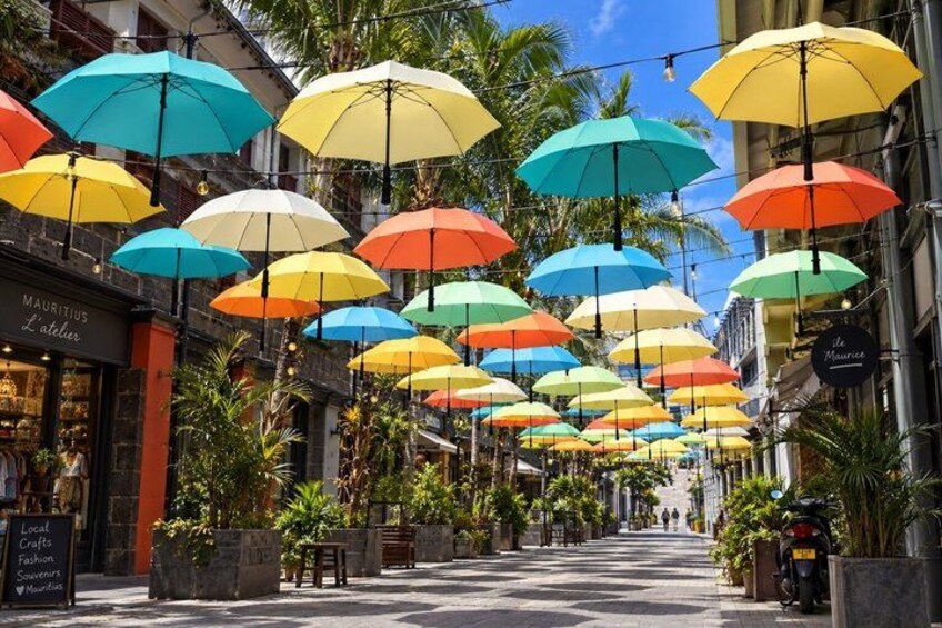 A street lined with colorful umbrellas, palm trees, and storefronts. 3