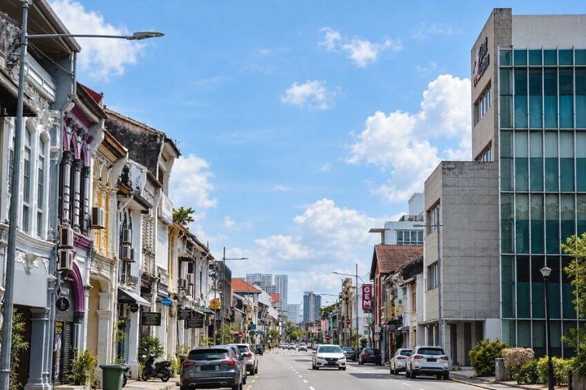 A street lined with historic buildings and modern architecture, vehicles parked along the road, and a clear sky. 4