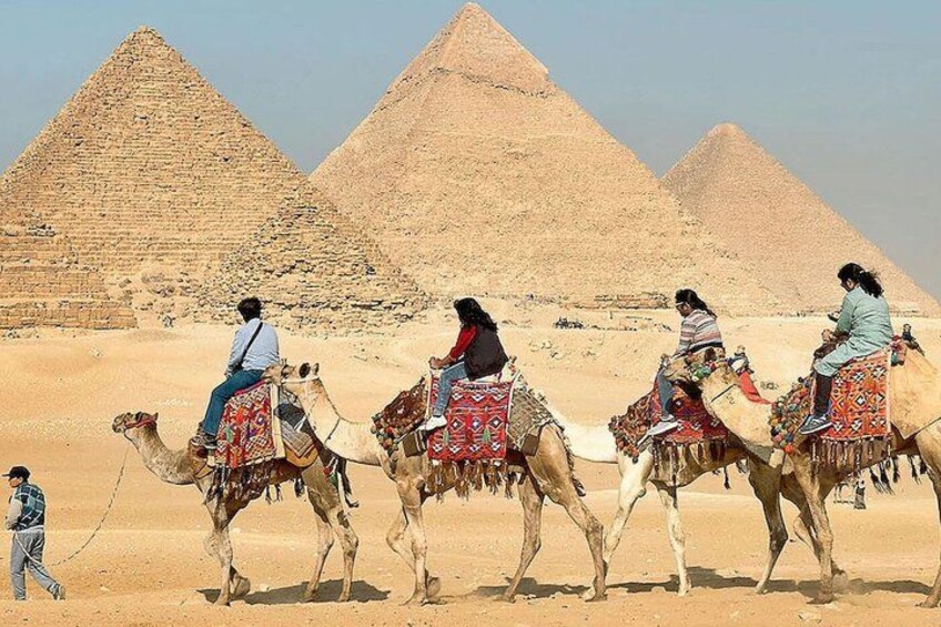 A desert landscape with pyramids in the background and people riding camels. 5