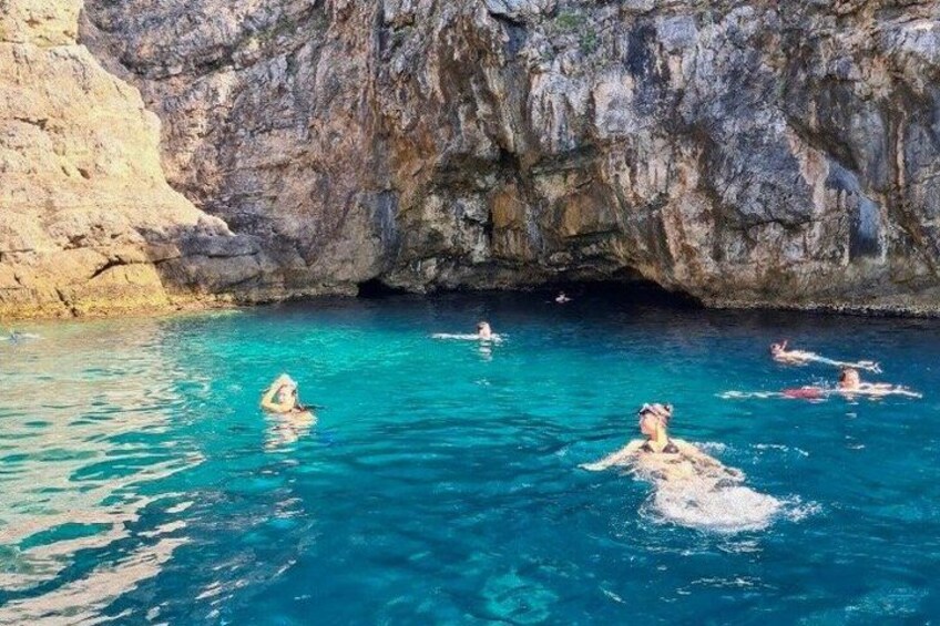 A group of people swimming in a clear blue sea with rocky cliffs in the background. 4