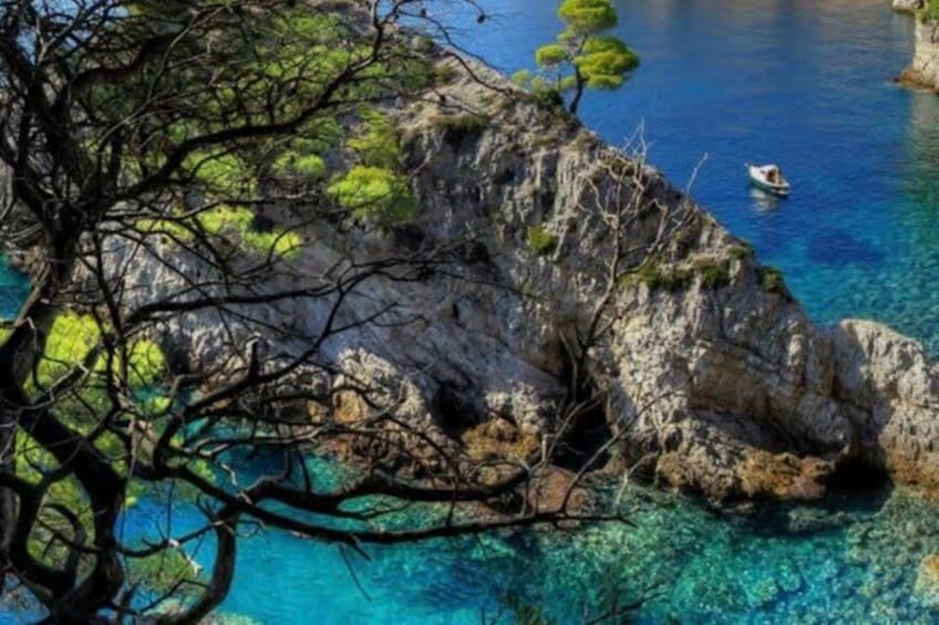 A rocky coastline with clear blue water, a small boat, and sparse vegetation. 2