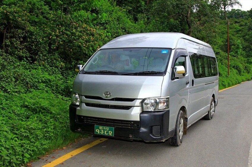 A silver van parked on a road with dense green foliage on both sides. 5