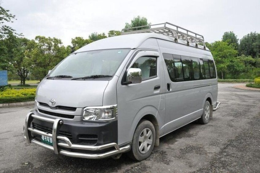 A silver van parked on a gravel surface with trees in the background. 1