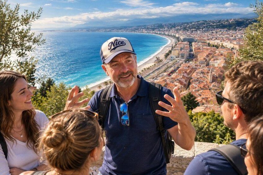 A group of people on a hill overlooking a coastal town with a beach and clear blue sea. 1