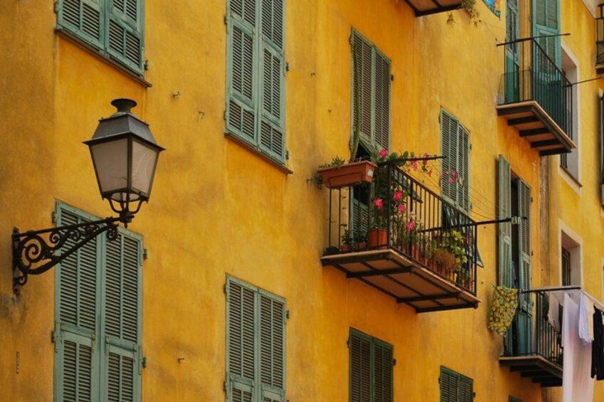 A yellow building with green shutters and a balcony with flowers. 2