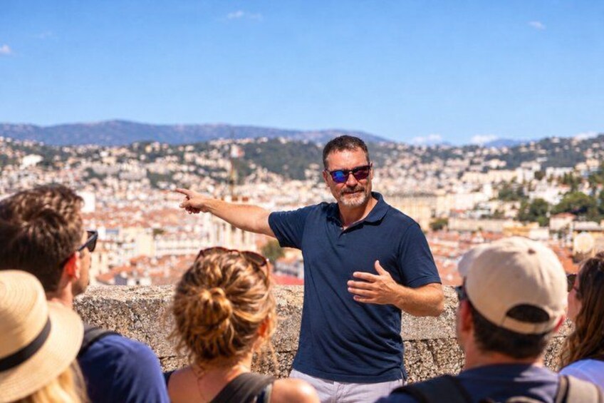 A man in a blue shirt pointing towards a cityscape with buildings and hills in the background. 5