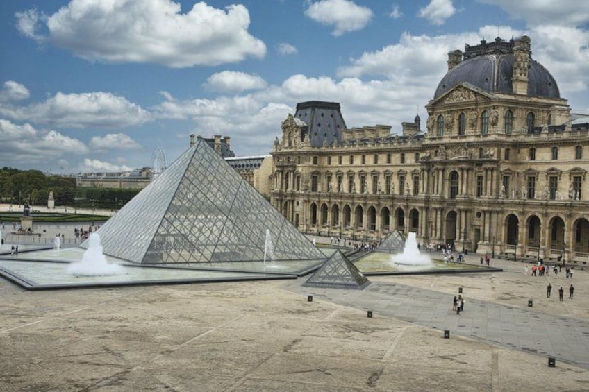 The Louvre Pyramid, a glass and metal structure, in front of the Louvre Museum's classical facade. 5