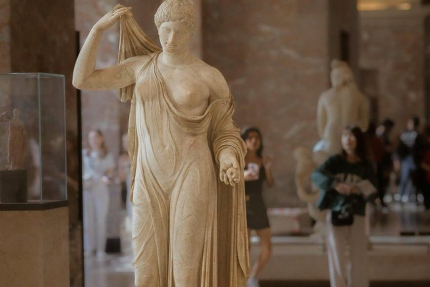 A marble statue of a woman in a museum with visitors in the background. 2