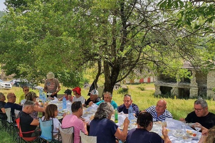 A group of people dining outdoors at a round table under a tree. 4