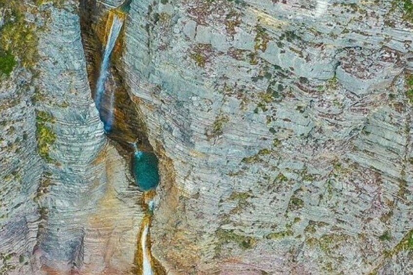 A canyon with layered rock formations and a small turquoise pool. 1