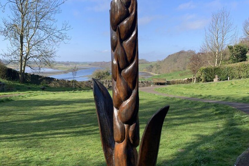 A sculpture of a twisted structure in a grassy field with a lake and hills in the background. 1
