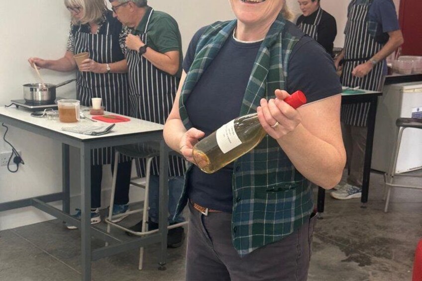 A person holding a bottle of wine in a kitchen setting with other people wearing aprons. 4