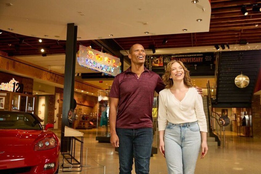 A man and woman standing in a shopping mall with a red car and a large illuminated sign in the background. 2