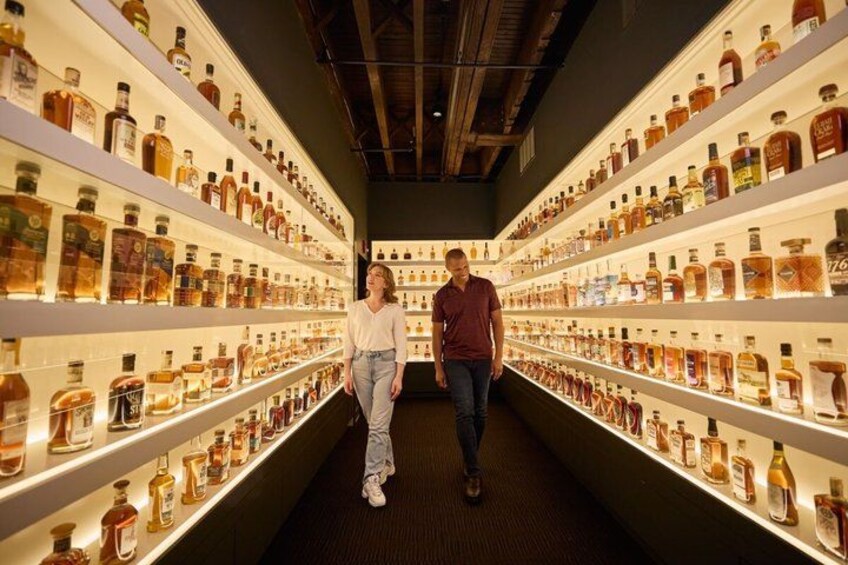A person walking through a store aisle with shelves of various liquor bottles. 5