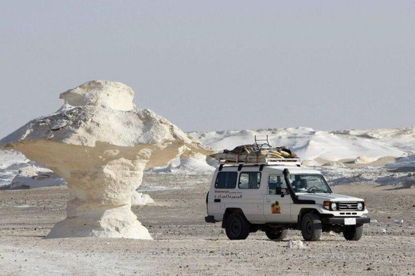 A white off-road vehicle parked near a large rock formation in a desert landscape. 4