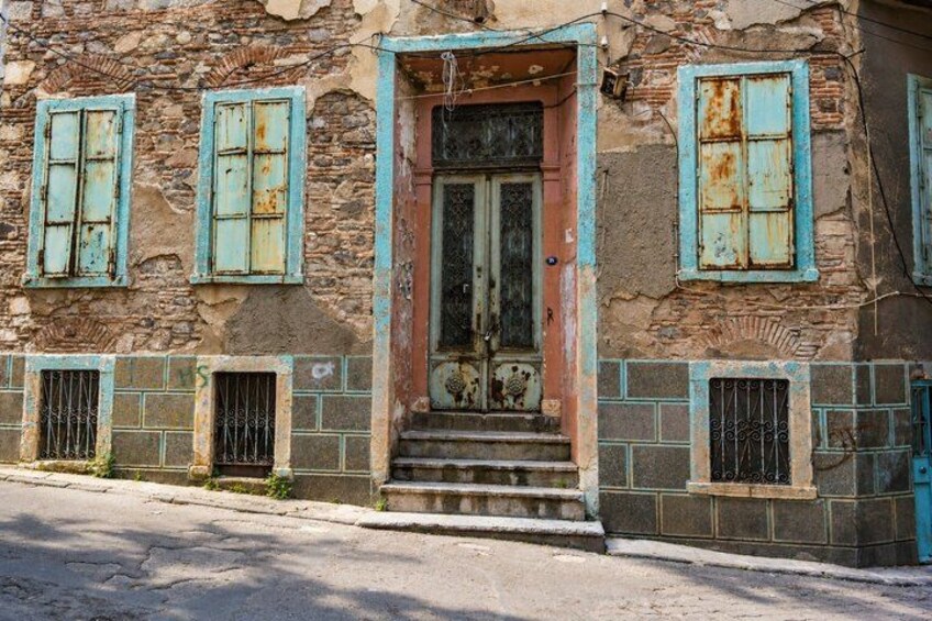 A weathered stone building with a worn wooden door and blue shutters. 3