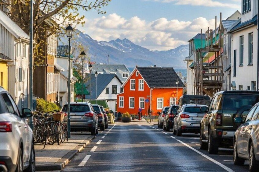A street with parked cars, a red house, and mountains in the background. 2