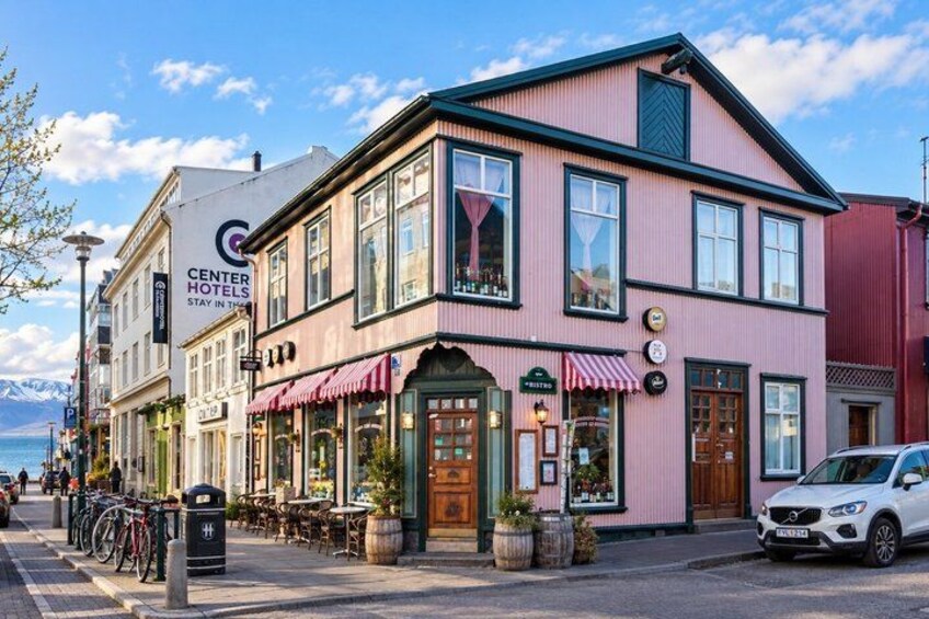 A pink building with a sign for Center Hotels, a storefront with a red awning, and a parked car. 4