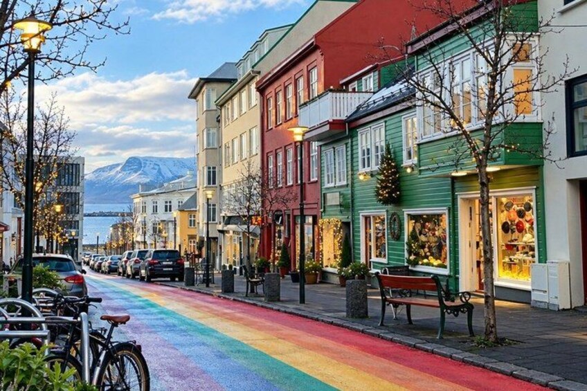 A rainbow-colored street with buildings, parked bicycles, and a bench. 3