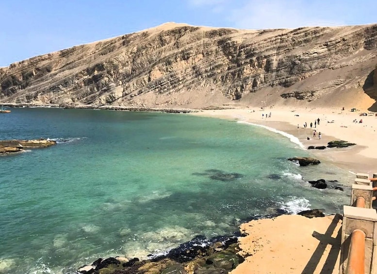 A coastal landscape with clear turquoise waters, a sandy beach, and rocky cliffs. 3