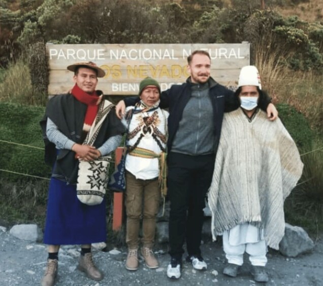 Un grupo de personas vestidas con atuendo tradicional posa frente a un cartel que dice 'Parque Nacional Natural Los Nevados'. 4