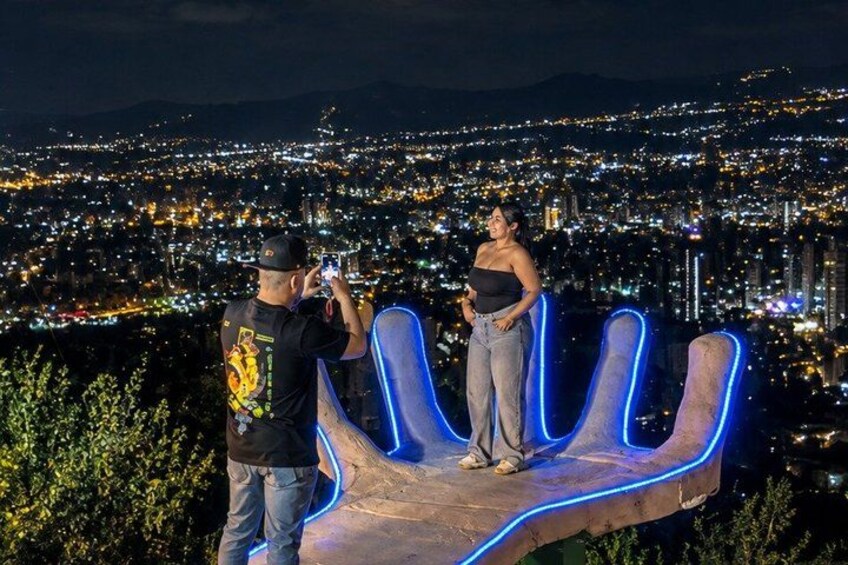 Two people standing on a rock formation with illuminated blue neon lights, overlooking a cityscape at night. 5