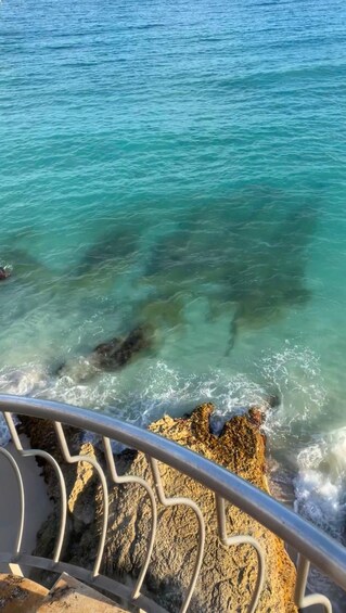 A coastal scene with clear turquoise water, rocky outcrops, and a metal railing. 3