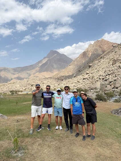 A group of people standing in a grassy field with mountains in the background. 4