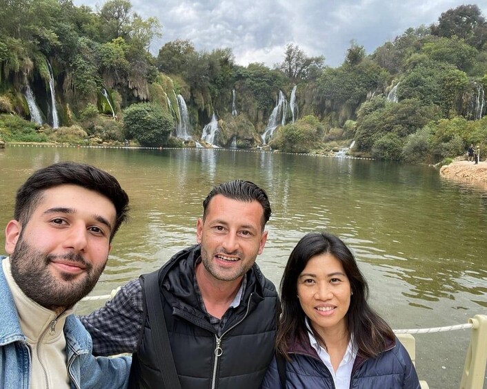 A group of people standing by a lake with waterfalls in the background. 4