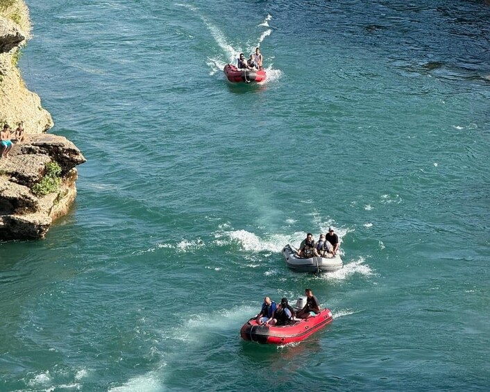 Three inflatable boats on a calm body of water with rocky cliffs on one side. 3