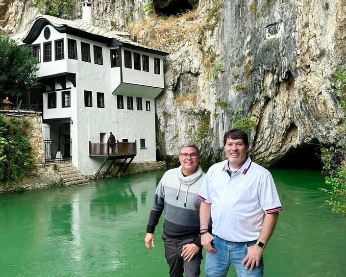 Two men standing in front of a building with a balcony overlooking a body of water. 2
