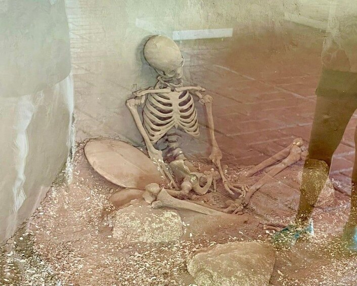 A skeleton in a seated position with a skull on the ground. 2