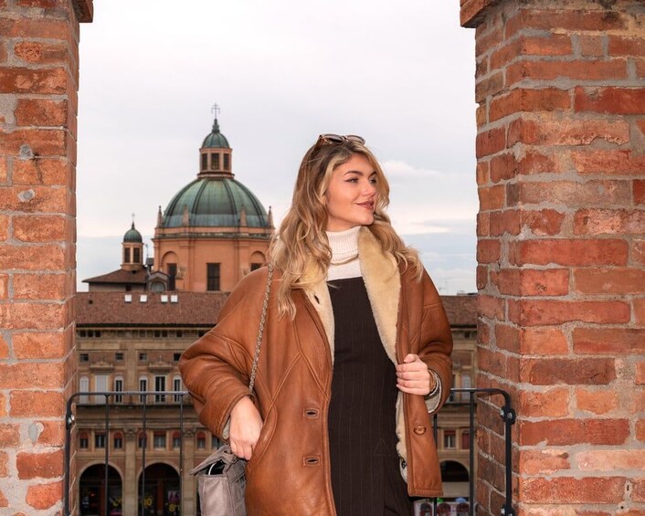 A person standing in front of a brick wall with a historic building featuring domes in the background. 1