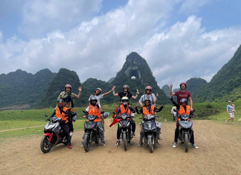 A group of motorcyclists in orange vests posing with their bikes in a hilly landscape. 1