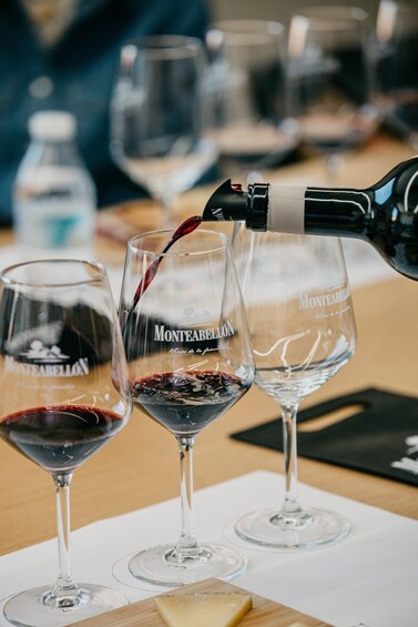 A wine bottle pouring red wine into a glass labeled 'Monteabellón' at a tasting event. 5