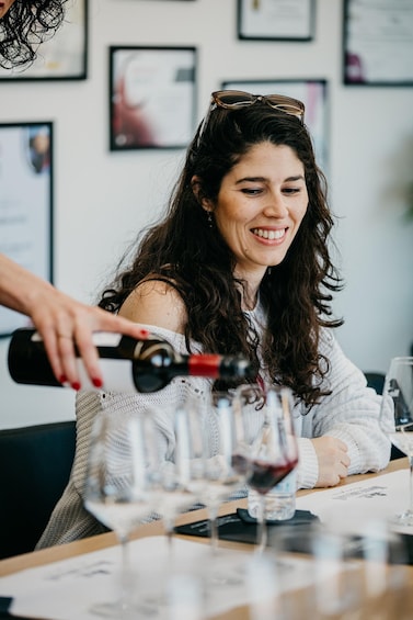 A person pouring wine into a glass at a table with multiple glasses and a bottle of wine. 4