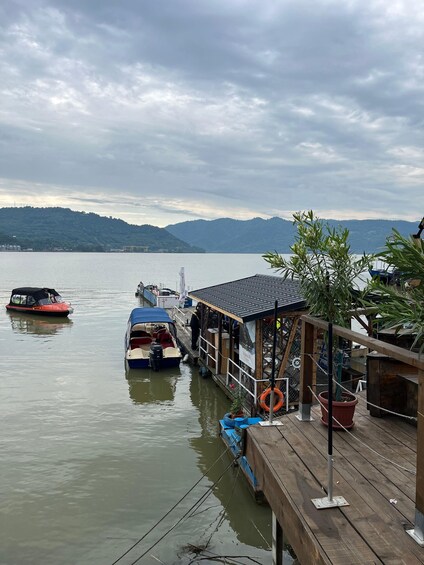A calm lake with boats docked at a wooden pier, surrounded by hills and a cloudy sky. 4