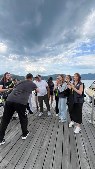 A group of people on a wooden dock by a body of water with a cloudy sky. 3