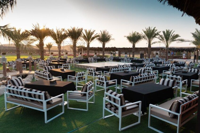 An outdoor seating area with tables and chairs, palm trees, and a sports field in the background. 2