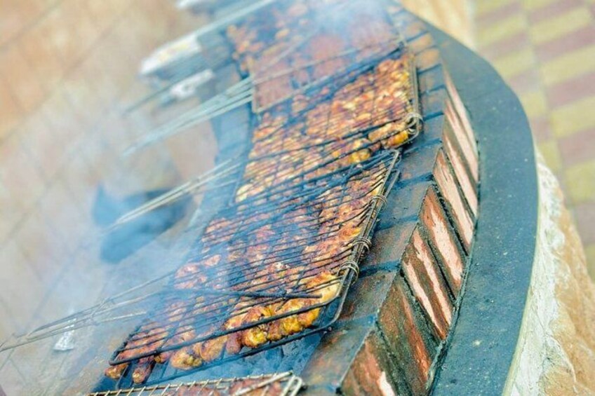 A long row of food being grilled on a metal rack over a brick oven. 4