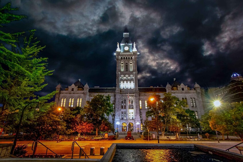 A historic building with a clock tower, illuminated windows, and a statue in front. 4