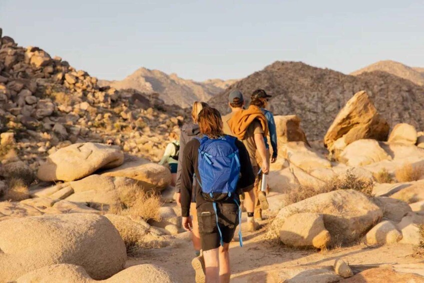 Un grupo de excursionistas caminando sobre un sendero pedregoso con grandes rocas y vegetación escasa. 2