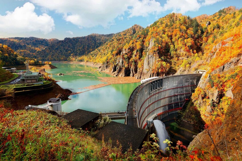 A dam with a spillway, surrounded by autumn-colored trees and a river. 1