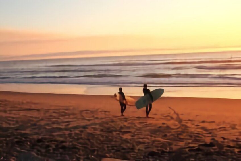 Two people walking on a beach with surfboards, ocean waves, and a sunset. 1