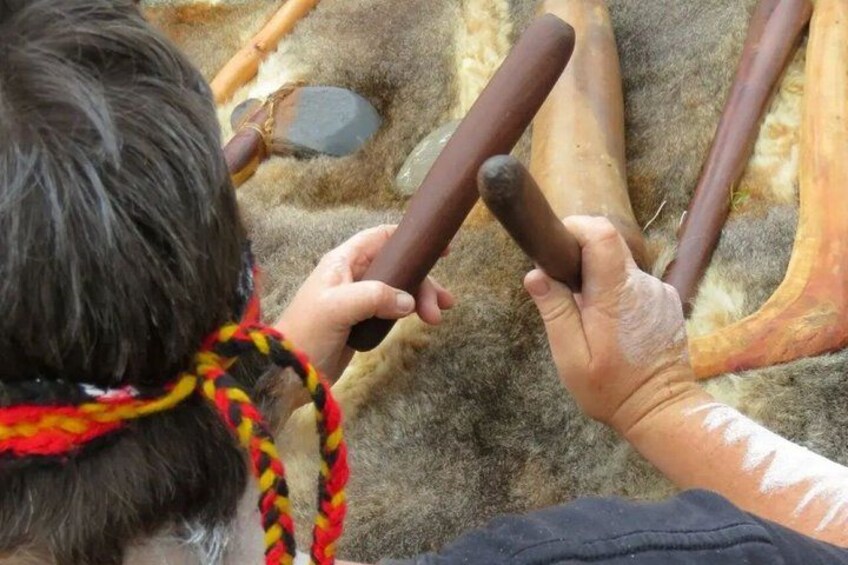 A person holding a wooden tool, possibly a hammer, with a fur-lined ground and a stone in the background. 4