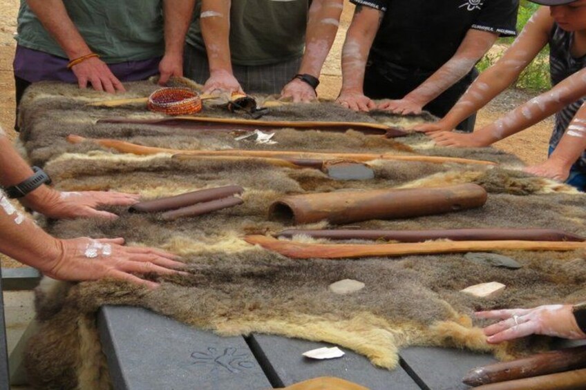A group of people handling large animal hides and tools on a table. 5