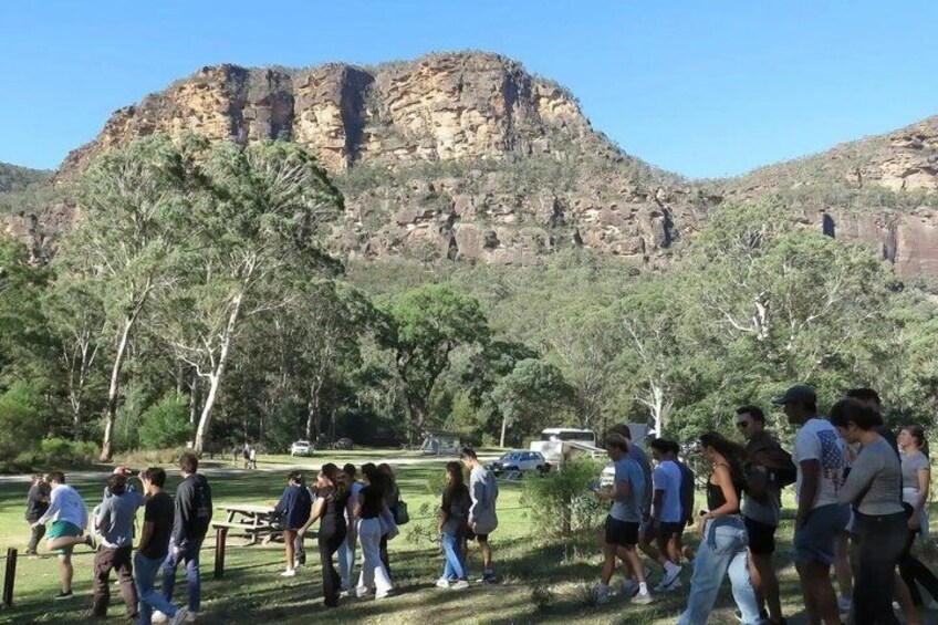 A group of people walking in a park with a large rock formation in the background. 2