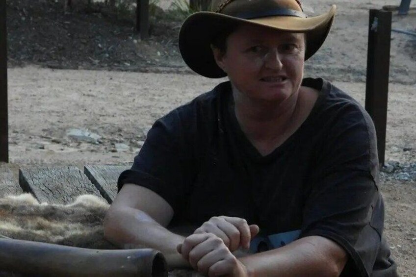 A person wearing a cowboy hat sitting on a wooden bench outdoors. 3